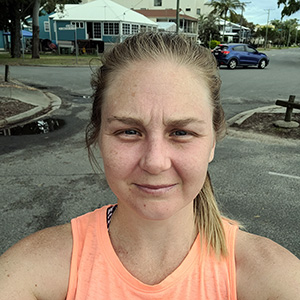 Alana standing in an apricot coloured running top. She is holding the camera to take a selfie and the sun is in her eyes