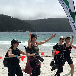 Hikers crossing the finish line. They are on a beach, celebrating their win with their arms outstretched. 
