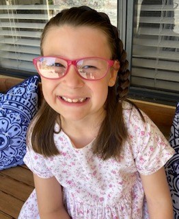 Adalynn smiling wearing a pink flowery dress and pick glasses