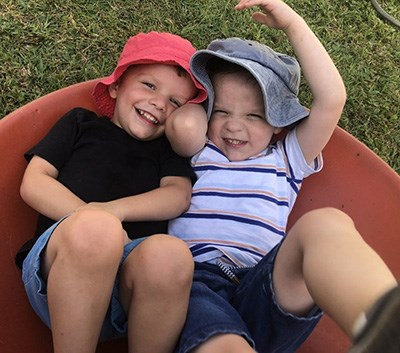 Xander with his brother smiling wearing matching sun hats